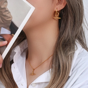 Detail of gold T-bar pendant necklace and matching earrings worn by a model