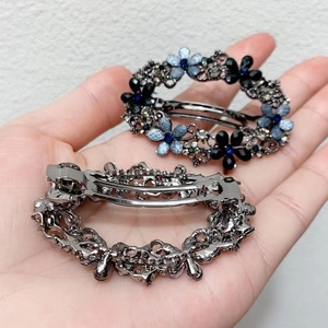 Detail of metal oval hair clips with blue rhinestones held in hand for scale
