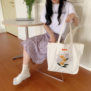 White canvas tote bag with floral embroidery and orange Solana tag held by model