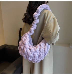 Detail of light purple ruched strap on a quilted cloud bag worn by a model in a trench coat