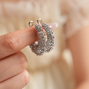 Macro shot of silver metal hoop earrings with sparkling pavé crystals held by hand