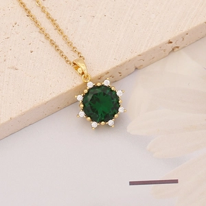Macro shot of gold-plated sunflower pendant with large emerald green cubic zirconia gem