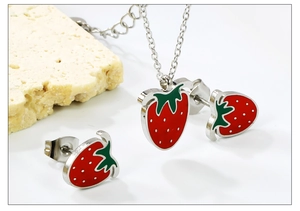 Macro shot of red strawberry pendant necklace and earrings set on a beige rock pedestal