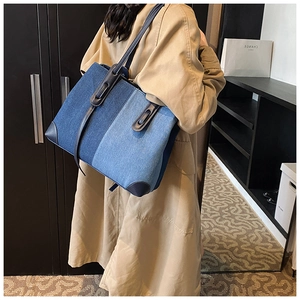 Detail of a large denim tote bag featuring blue patchwork design and leather handles