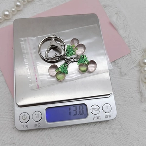 Detail showing pink translucent cherry keychain on scale weighing exactly 13.8g