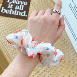 Detailed close-up of a white organza scrunchie with red and blue polka dots on hand