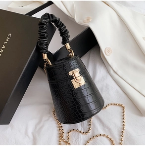 Detail of black crocodile texture bucket bag with gold chain and pleated handle on gift box