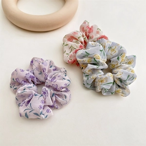 Close-up of three floral chiffon hair scrunchies in pink, purple and blue pastel colors