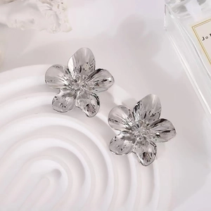 Large silver floral stud earrings with textured petals on minimalist display stand