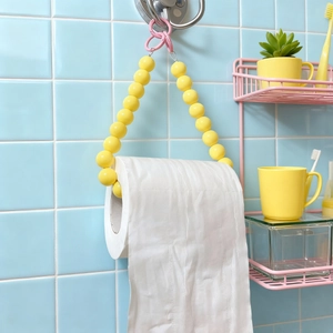 Detail of yellow beaded toilet paper holder with a pink hook on blue tiles