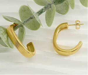 Macro detail of gold C-shape stud earrings with ribbed texture on a white tray