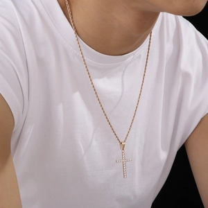 Détail d'un collier croix en or rose avec diamants sur un mannequin portant un t-shirt blanc