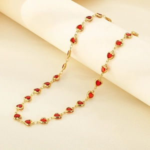 Detail of a gold necklace featuring red heart-shaped glass gemstones on a white pedestal