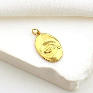 Gold oval pendant with embossed eye design on white stone surface for DIY jewelry making