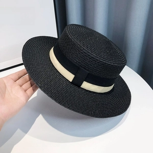 Close-up of black straw boater hat featuring a cream ribbon and elegant side bow detail