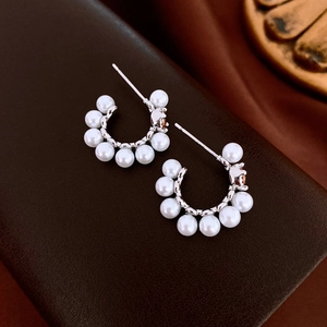 Detailed close-up of C-shaped pearl earrings with silver metal base on leather
