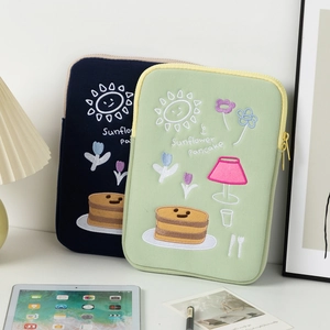 Detail of embroidered laptop sleeves in navy and green with sunflower pancake patterns