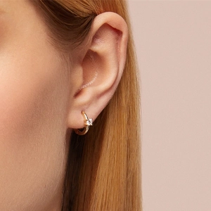Detailed close-up of a 925 silver golden twisted hoop earring with a sparkling clear zircon