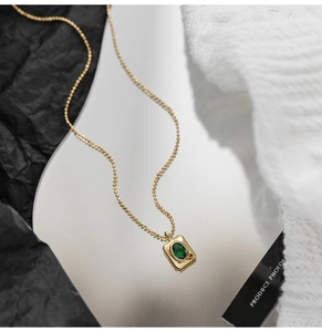 Detailed macro view of an elegant gold ball chain necklace with a green crystal pendant