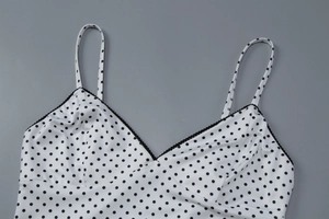 Detail of white polka dot camisole with black wavy trim and V-neckline fabric texture