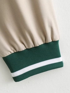 Detail view of beige jacket featuring dark green and white striped ribbed cuffs texture
