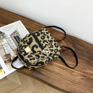 Detailed view of leopard print mini backpack with canvas texture and gold hardware on wood