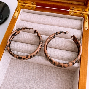 Close-up of leopard print hoop earrings on a gray textured jewelry box display