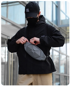 Gray geometric hardshell chest bag worn by male model against modern glass wall background