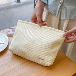 Detail of a beige corduroy cosmetic bag held by a model in a cozy cafe setting