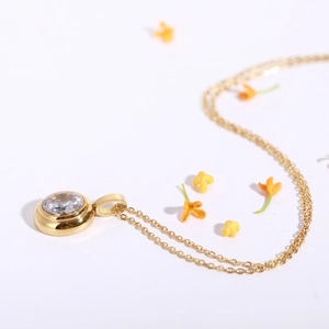 Detail of a 18k gold plated necklace featuring a round clear crystal pendant on white background