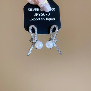 Detailed view of silver knot earrings with pavé zircon and a dangling white pearl charm