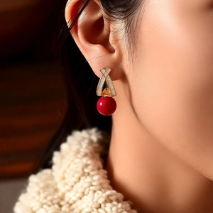 Macro view of 18k gold plated earring with zircon X-shape and large red bead on a model