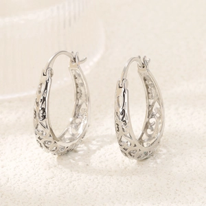 Macro shot of silver hollow-out geometric oval hoop earrings with intricate floral patterns