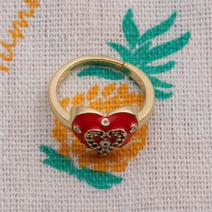 Macro detail of gold plated heart ring with red enamel and devil eye zircon inlay