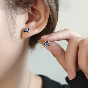 Elegant gold evil eye stud earrings with blue enamel finish worn by a model