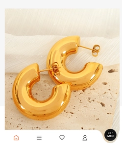 Close-up of golden C-shaped hoop earrings on elegant beige stone and fabric