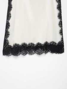 Detailed close-up of white satin fabric with intricate black lace trim and floral patterns