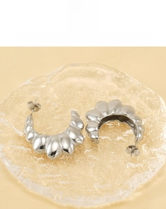 Macro shot of silver C-shaped wave textured earrings on ice-cracked glass surface
