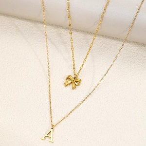 Macro shot of double-layered gold necklace featuring a bow pendant and letter A charm
