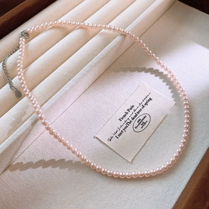 Detail of a pink pearl necklace on beige velvet display with vintage aesthetic card