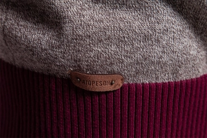 Detail von grauem und weinrotem Strickgewebe mit Leder-Markenaufnäher am Saum