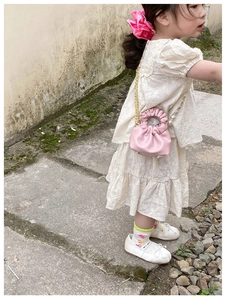 Pink pleated mini bucket bag with pearl strap shown on a child model outdoors