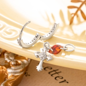 Silver hoop earrings with cross pendant and orange marquise gem on a beige plate