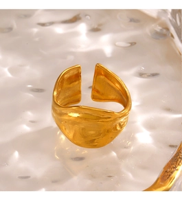 Close-up of a chunky irregular gold ring with a textured finish on a glass surface