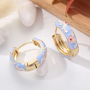 Light blue enamel hoop earrings with pink flower patterns on a natural wood background
