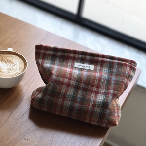 Detail of plaid tweed cosmetic bag with Simple Wish label on wooden table with coffee