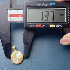 Macro shot of a digital caliper measuring a 13.7 mm round gold pendant with heart shells