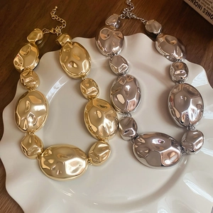 Close-up of gold and silver chunky oval textured link necklaces on a white plate