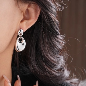 Macro shot of silver irregular oval metal earrings with a glossy polished texture