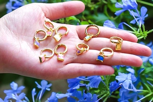 Detailed shot of colorful enamel lock pendants on gold hoops held in a hand